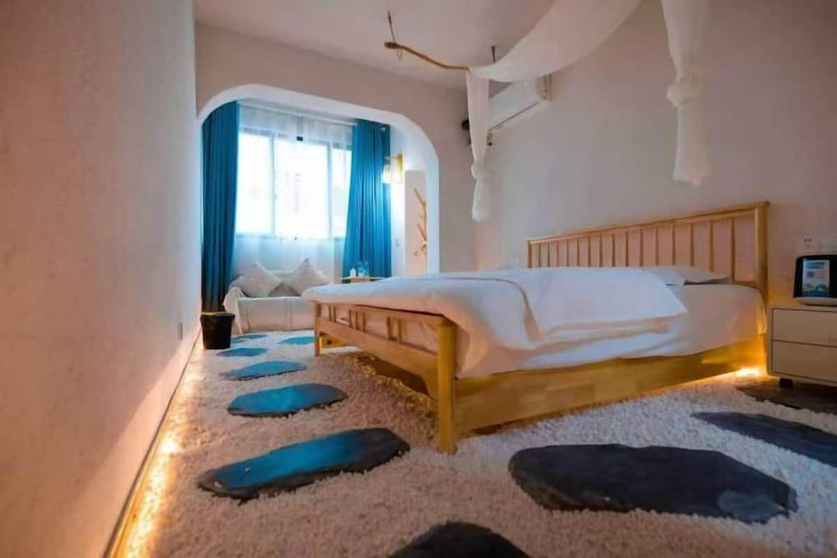 Un dormitorio con cama, mesita de noche, una silla y ventana con cortinas.
