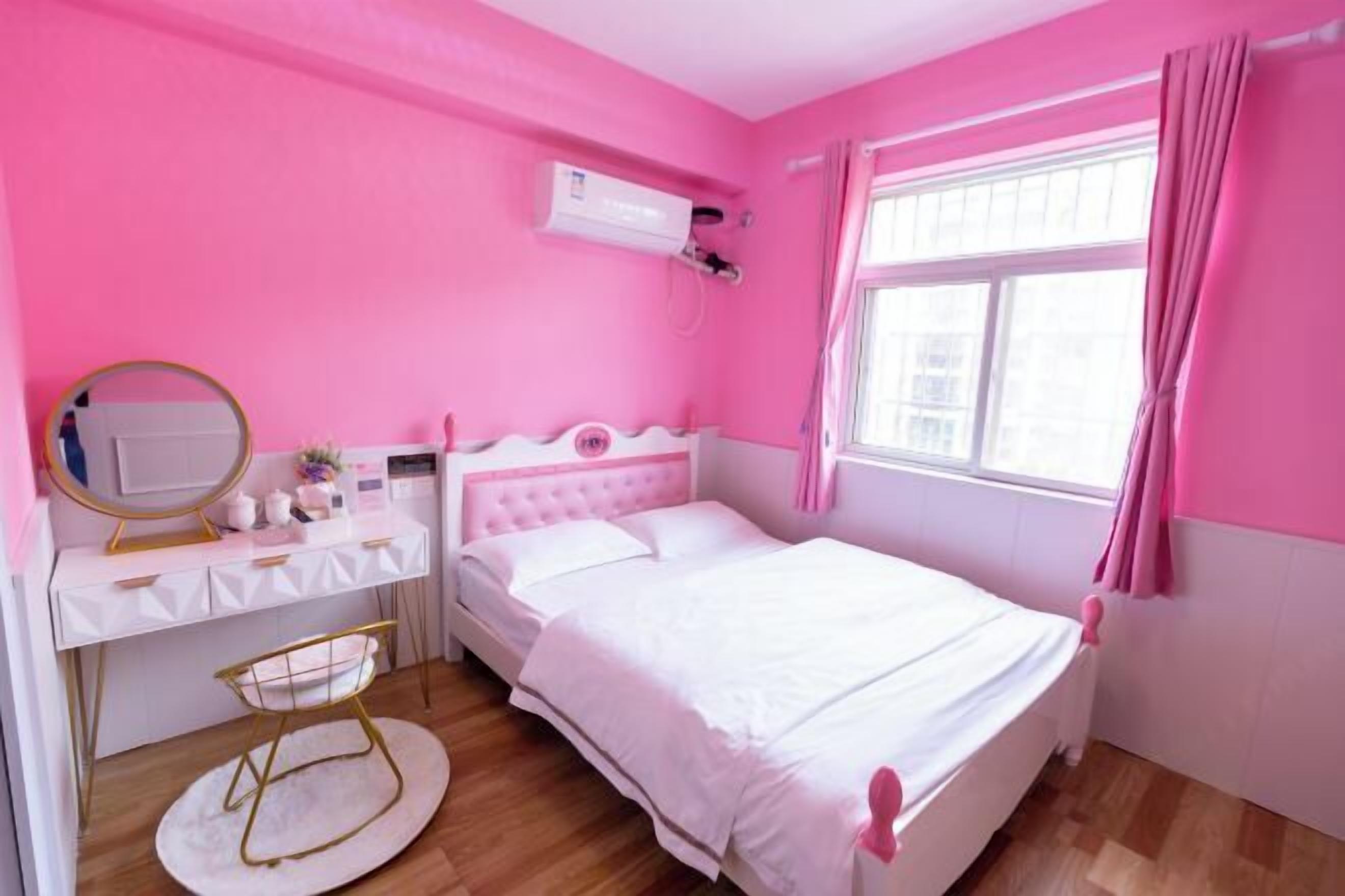 Un dormitorio con temática rosa, que incluye una cama, un tocador con espejo y una ventana con cortinas.