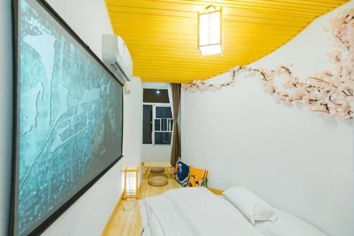 Una habitación con una cama, aire acondicionado instalado en la pared, una ventana y un proyector también instalado en la pared.