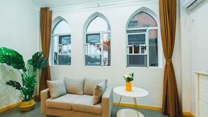A room with a beige sofa, a small round table with a vase, and a large potted plant.