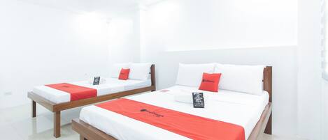 Dos camas individuales con cabeceros de madera y ropa de cama blanca, cada una con una almohada roja de detalles y una almohada con la marca RedDoorz.