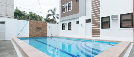 A swimming pool with a clear blue water feature, surrounded by a light-colored tiled deck.