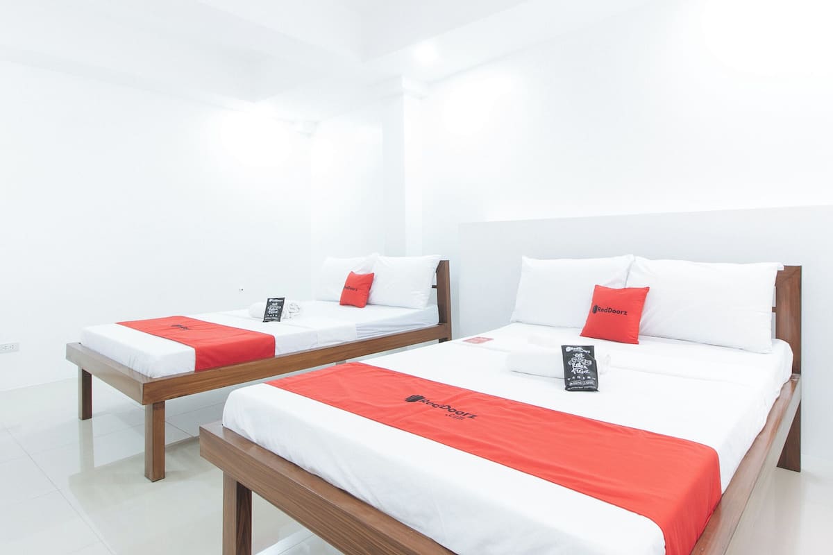 Two single beds with wooden frames and white bedding, each with a red accent pillow and a RedDoorz branded pillow.