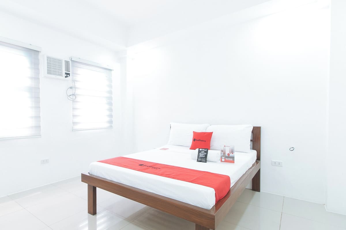 A modern hotel room with a wooden bed, white bedding, and a red accent pillow.