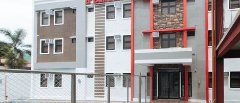 A building with a sign reading "RedDoorz of Builders Rooms" and a swimming pool in the foreground.