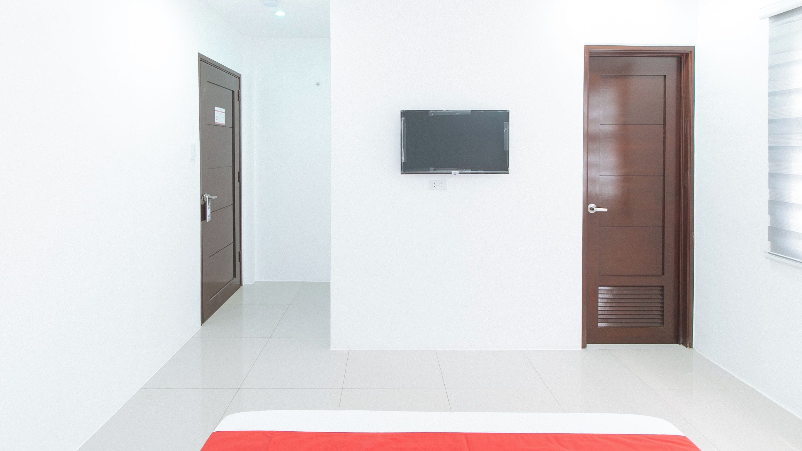 Una habitación de hotel con una cama, un televisor montado en la pared y dos puertas.