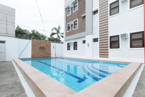 A swimming pool with a clear blue water feature, surrounded by a light-colored tiled deck. - Reddoorz Plus @ D'builders Poblacion - Bgc (Taguig)