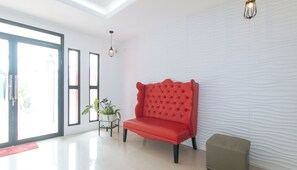 A spacious room with a red sofa, a small table with a plant, and a large window with blinds. - Reddoorz Plus @ D'builders Poblacion - Bgc (Taguig)