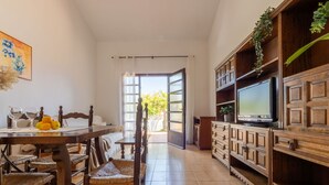 Ein Essbereich mit Holztisch und -stühlen, einem Fernseher auf einer Holzkommode und Blick ins Freie durch eine offene Tür.