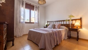 Ein Schlafzimmer mit einem Bett, einem Nachttisch, einer Lampe, einem Fenster mit Vorhängen und einem Holzschrank.