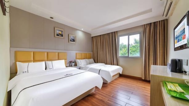 Habitación de hotel con dos camas, suelo de madera, escritorio y ventana con cortinas.