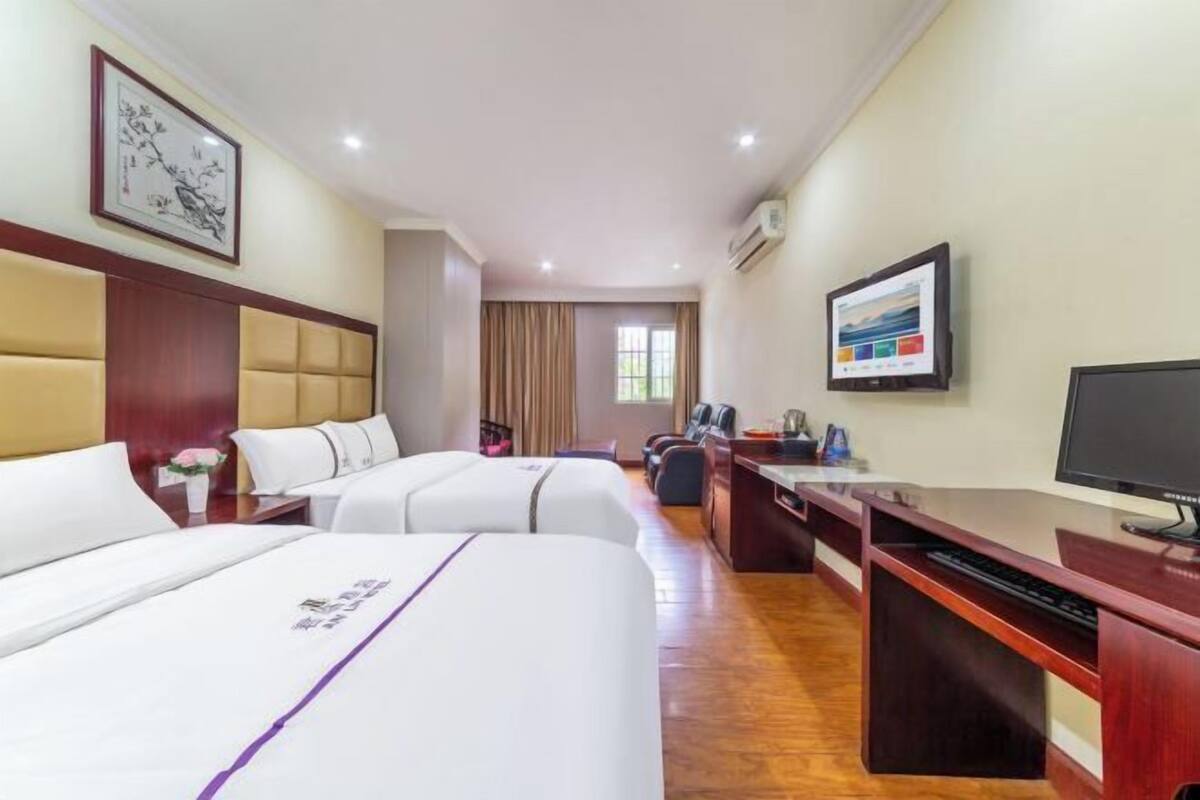 Una habitación de hotel con dos camas, un escritorio con una computadora, un televisor y un ventanal grande.