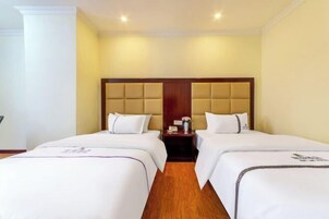 A hotel room with two beds, a wooden headboard, and a nightstand with a lamp.