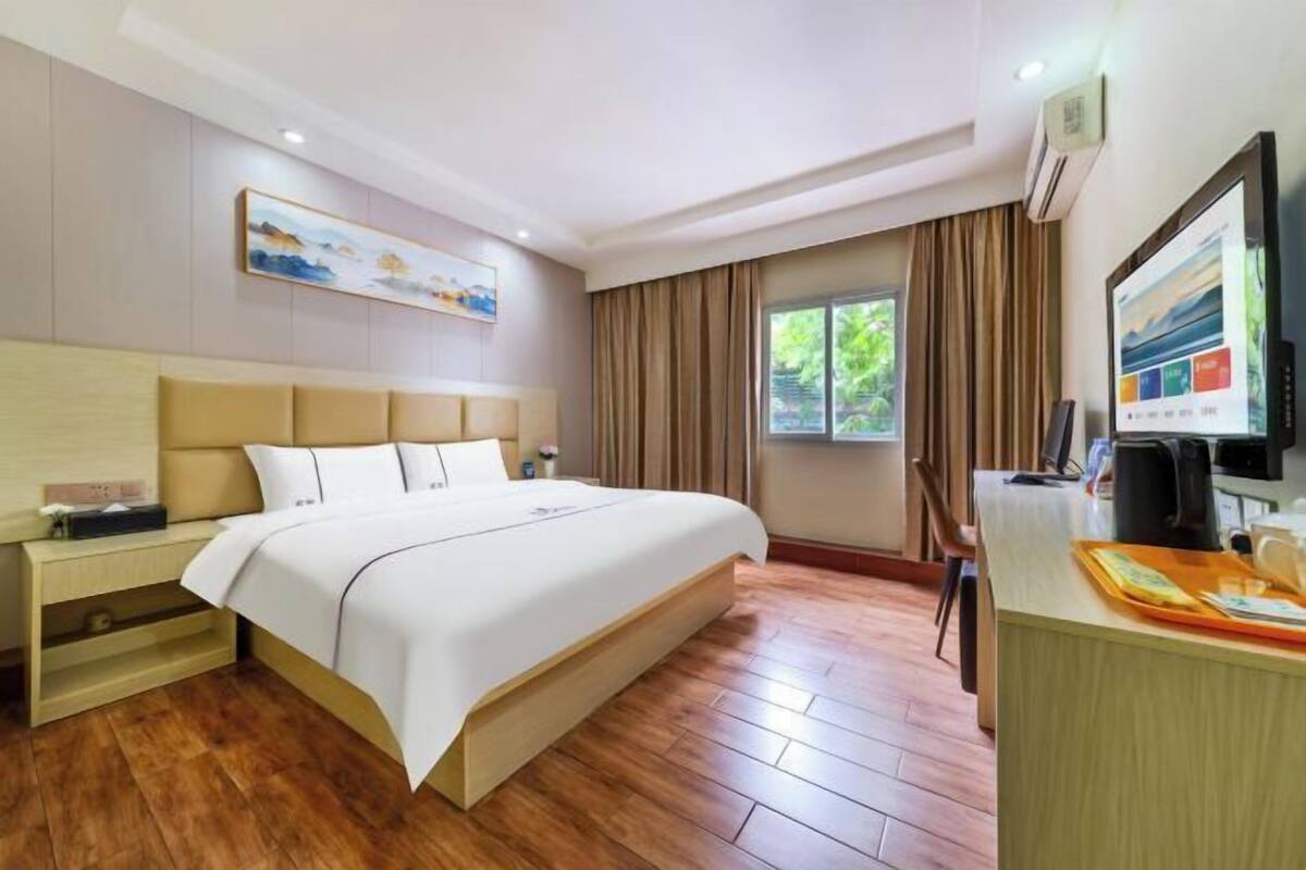 Habitación de hotel con cama, mesita de noche, televisor y ventana con cortinas.