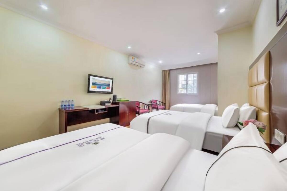 Habitación de hotel con dos camas, un escritorio con una silla, una mesita con botellas de agua y un cuadro en la pared.
