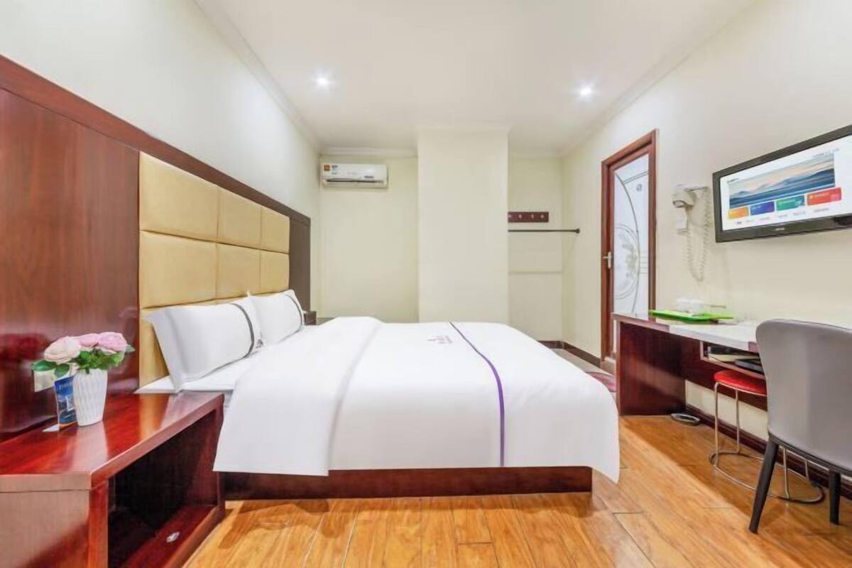 Habitación de hotel con cama, escritorio, silla, televisor y aire acondicionado.