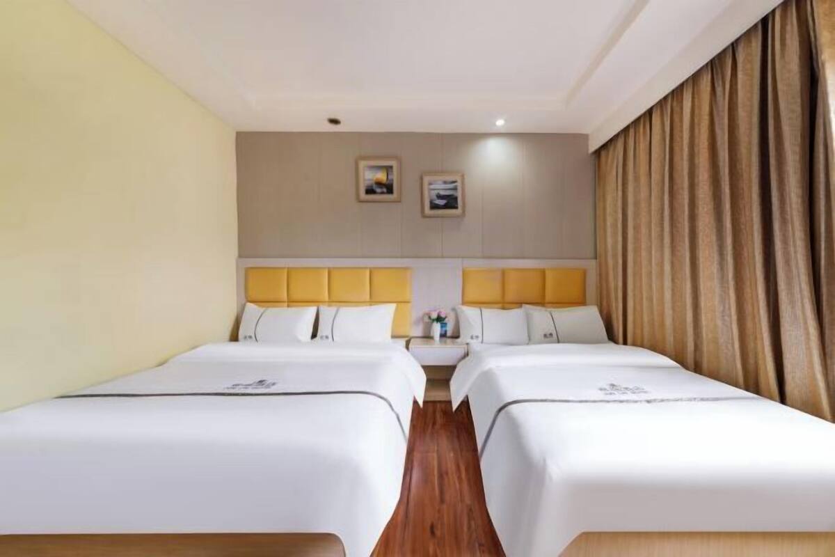 Habitación de hotel con dos camas, piso de madera, pared color crema y una cortina a la derecha.