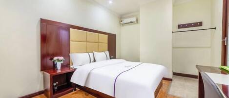 A hotel room with a wooden headboard, a bed with white bedding, a small bedside table with a vase of flowers, and a wooden floor.