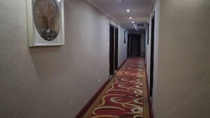Un pasillo con alfombra estampada, cuadros en la pared y puertas que dan a varias habitaciones.