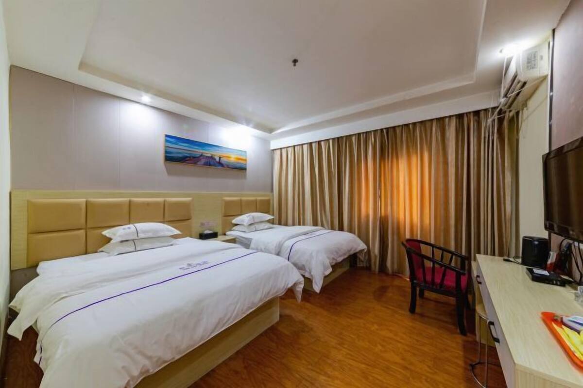 Habitación de hotel con dos camas, un escritorio, una silla, un televisor y un cuadro en la pared.