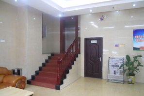 Un vestíbulo con una escalera, una recepción, una puerta y un cartel en la pared.