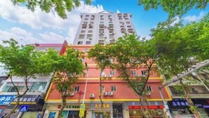 Un edificio de varios pisos con fachada roja, varias tiendas a nivel de calle y árboles en la parte delantera.