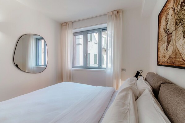 A bedroom with a bed, a window with curtains, a round mirror, and a wall-mounted map.