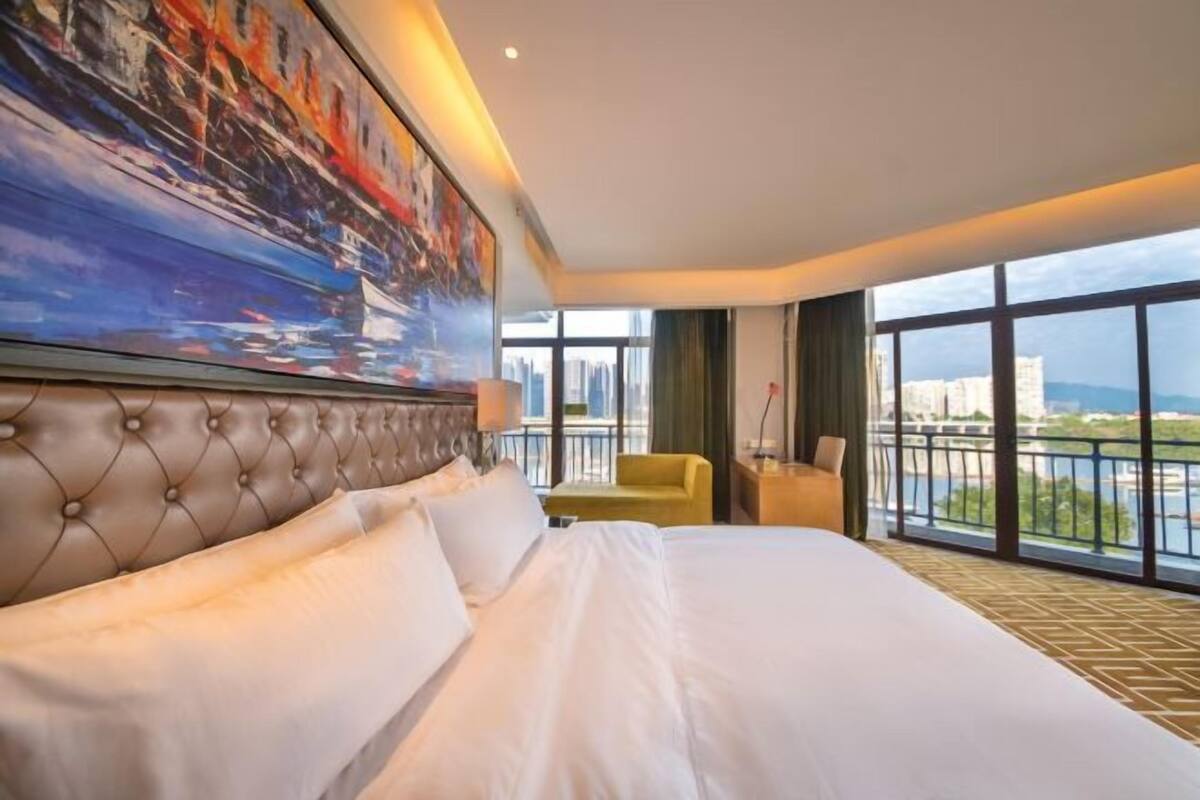 Une chambre d’hôtel avec un grand lit, un tableau au mur, un balcon avec vue et un fauteuil.