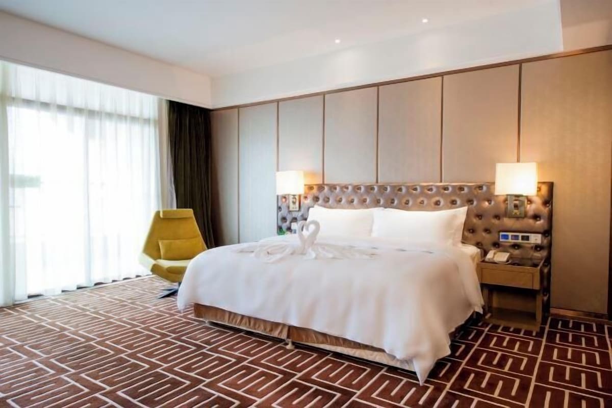 A hotel room with a large bed, a nightstand, a lamp, and a chair.