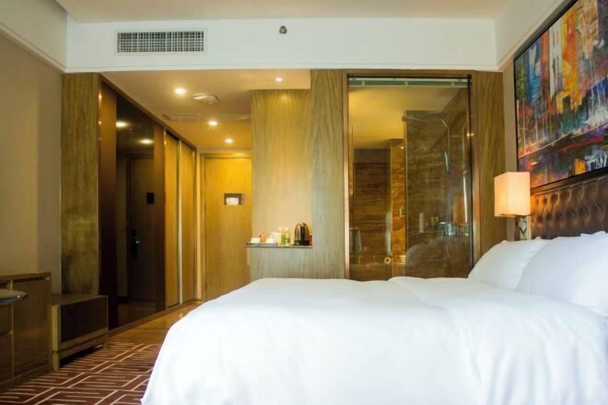 Une chambre d’hôtel avec un grand lit, une salle de bain dotée d’une douche en verre et un tableau accroché au mur.