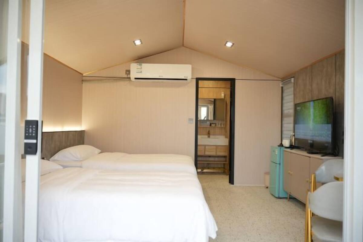 Une chambre d’hôtel avec deux lits, une télévision, un minibar et une salle de bain équipée d’un miroir et d’un lavabo.