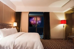 A hotel room with a bed, a nightstand, a lamp, a window with curtains, and a patterned floor. - Jinkai Shengyucheng Hotel Sihui (Sihui)