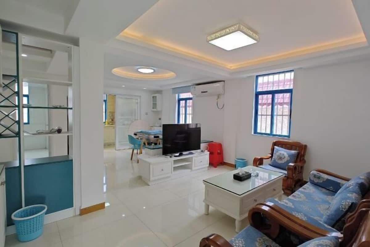 A modern living room with a sofa, a coffee table, a TV, and a kitchen area in the background.