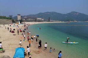 Una playa con gente, un faro y montañas al fondo.