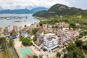 Un pueblo costero con edificios residenciales, una cancha de baloncesto y vistas al mar y a las montañas.