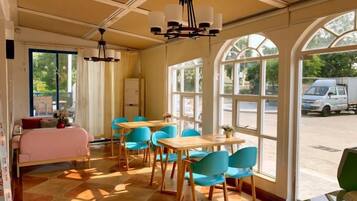 A room with a bed, a dining table, chairs, and large windows.