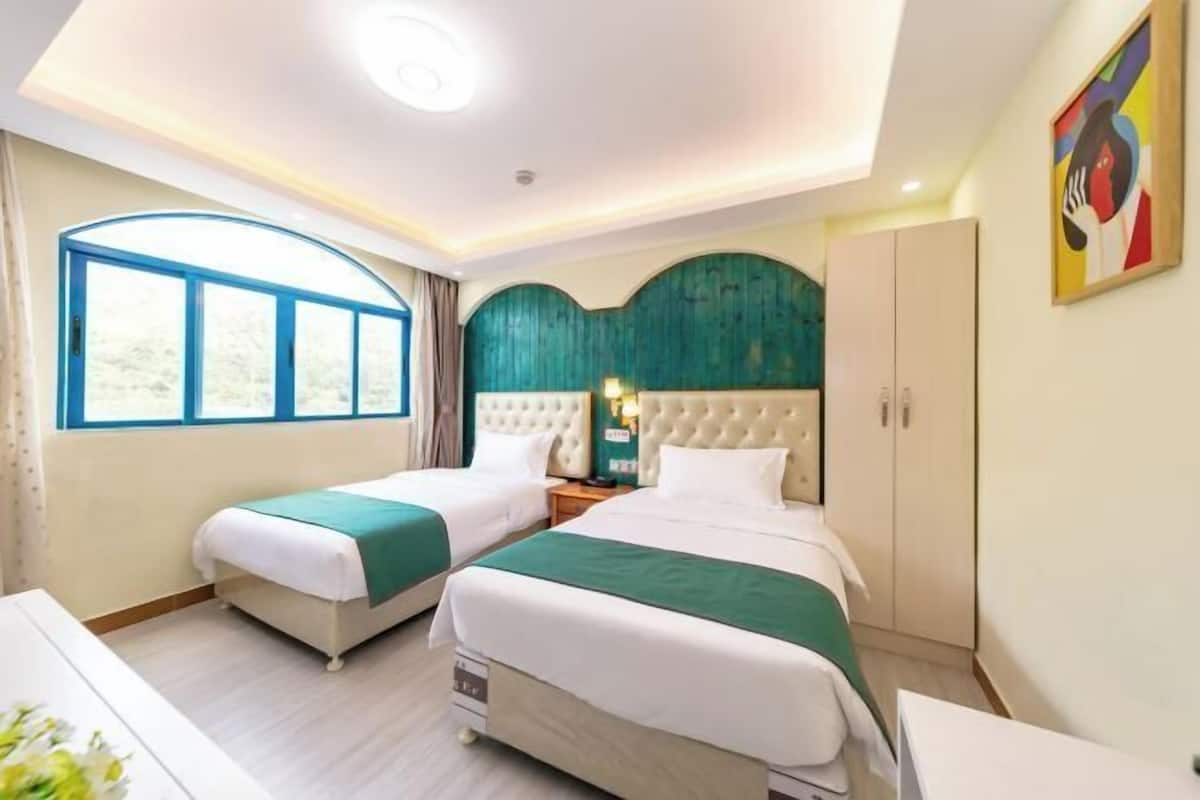 A hotel room with two beds, a large window, a decorative wall, and a cabinet.