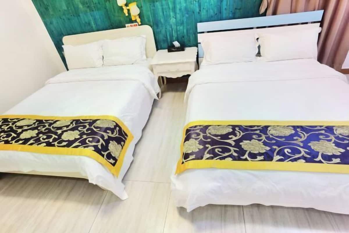 Two single beds with white bedding and decorative blue and gold bedspreads, a white nightstand between them, and a teal-colored wall.