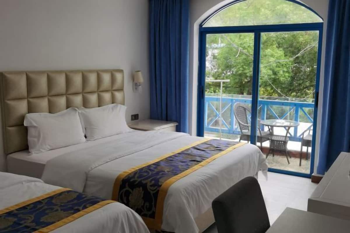 A hotel room with a large bed, a desk, and a balcony with chairs.