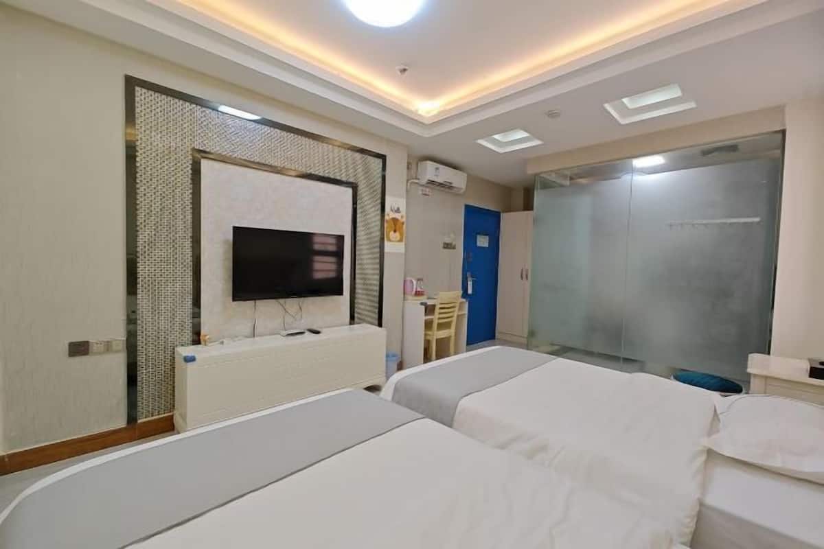 A hotel room with two beds, a TV, a shower, and a small table.