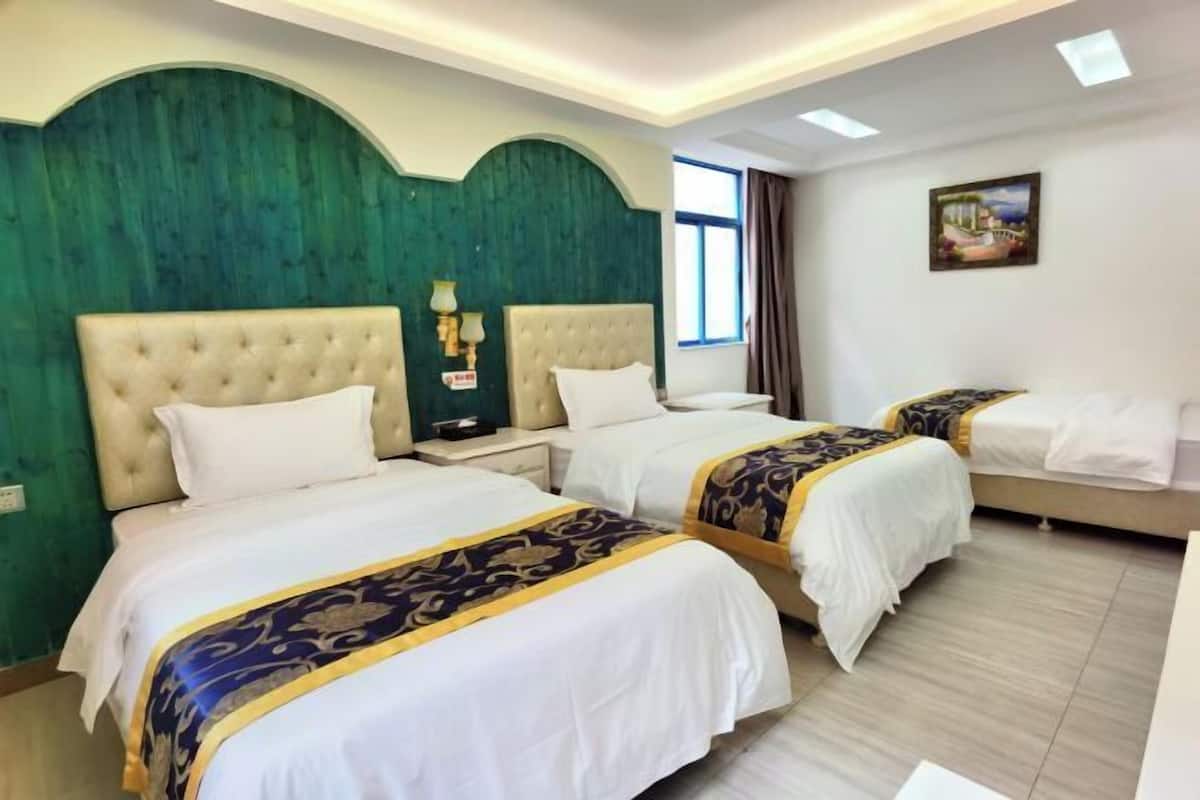 A hotel room with three beds, each with a white and blue bedspread, a green accent wall, and a painting on the wall.