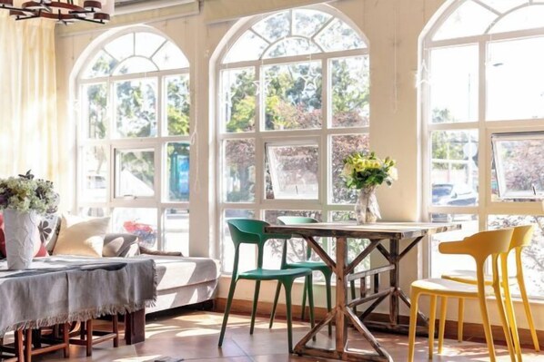 Una habitación iluminada por el sol con una mesa y sillas, ventanas amplias y vistas al exterior.