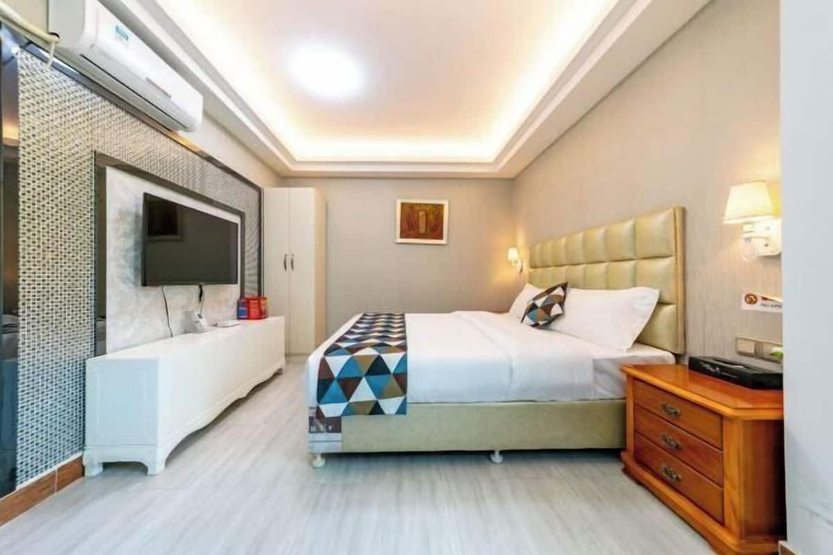 A modern hotel room with a bed, bedside table, TV, and a wall-mounted air conditioner.