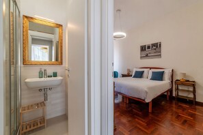 Ein Hotelzimmer mit Holzboden, einem Bett mit weißer und blauer Bettwäsche, einem Nachttisch mit Lampe und einem an der Wand befestigten Spiegel.