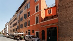 A row of buildings with a café on the ground floor, parked cars, and a clear sky. - Apartment with Terrace on the Vatican Passetto (Roma)