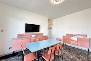 A modern dining area with a blue table and orange chairs, a flat-screen TV mounted on the wall, and a pink and white color scheme.