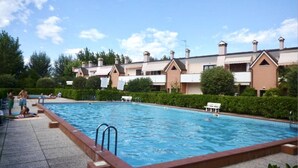 A swimming pool with a tiled deck, surrounded by a row of buildings with pitched roofs and chimneys.