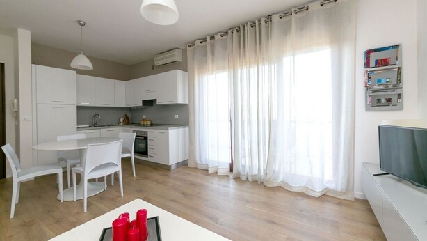 A modern kitchen with white cabinets, a dining table with chairs, and a TV on a cabinet.