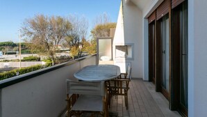 A balcony with a round table and chairs, a view of the street, and a building with large windows.