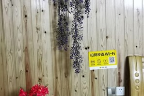 A wooden wall with a sign indicating Wi-Fi availability, a power outlet, and a decorative plant.